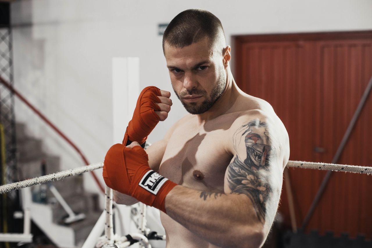 a tattooed male boxer in the gym with hand wraps showing determination