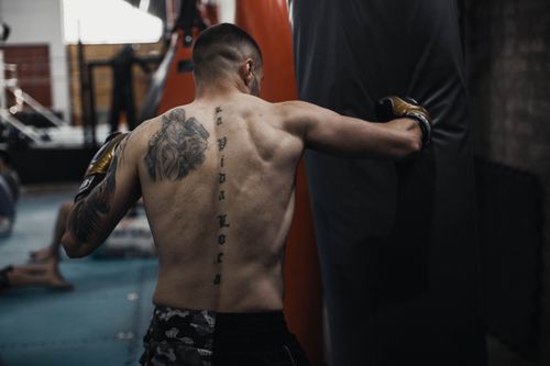 Free A shirtless male athlete practicing boxing techniques on a punching bag indoors. Stock Photo