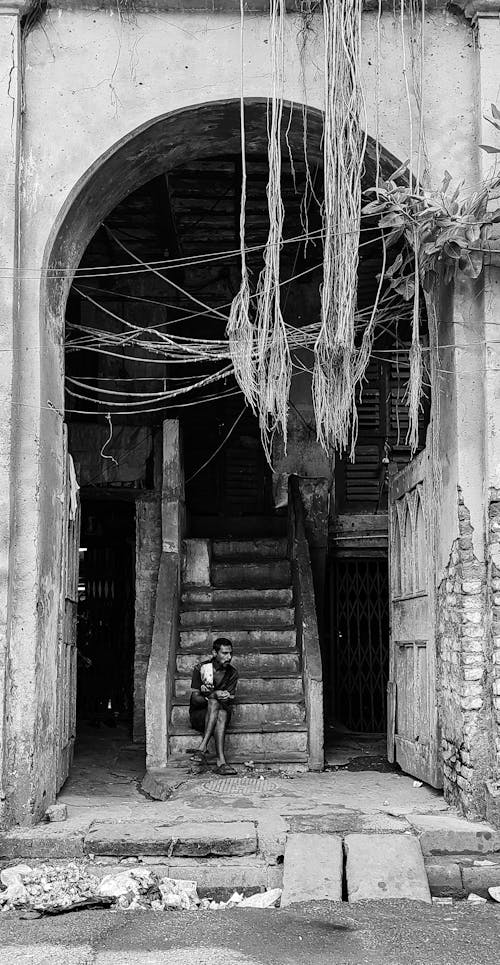 Grayscale Photo of a Man Sitting on Concrete Stairs