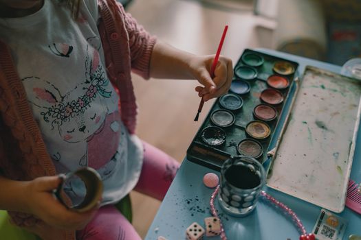 A young child painting with watercolors, wearing a cute printed shirt, engaging in creative art at home.