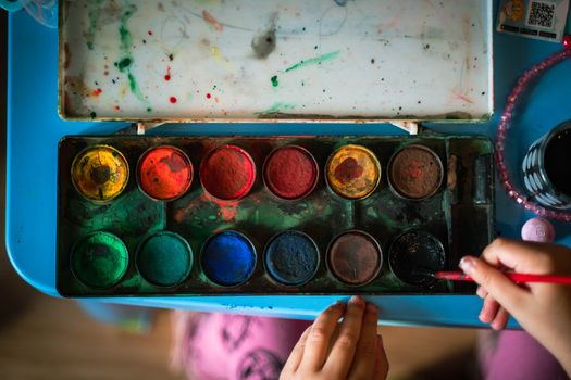 Top view of vibrant watercolor paints and brush in use on a blue surface.