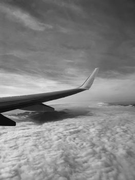 A dramatic black and white view of an airplane wing soaring above fluffy clouds.