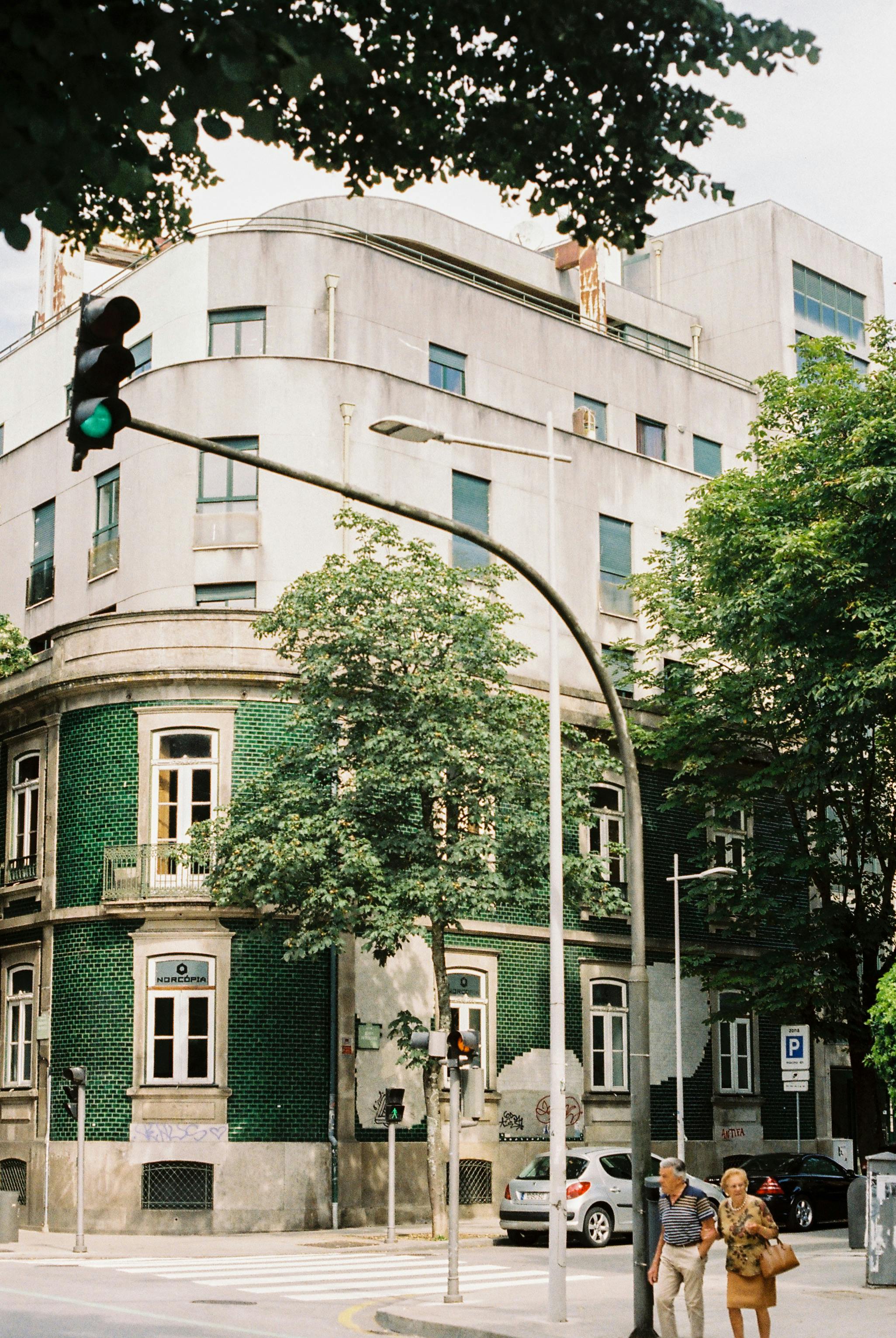 A charming street scene in Porto, Portugal, featuring a green facade building and two pedestrians crossing.