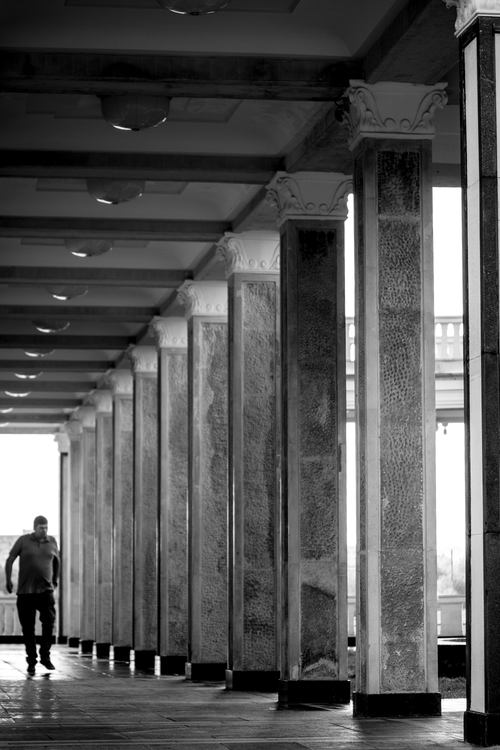 Free Black and white photo of a man walking through a columned hallway. Stock Photo