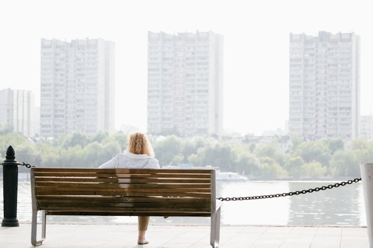 A Woman Sitting On A Bench With A View Of A Lake