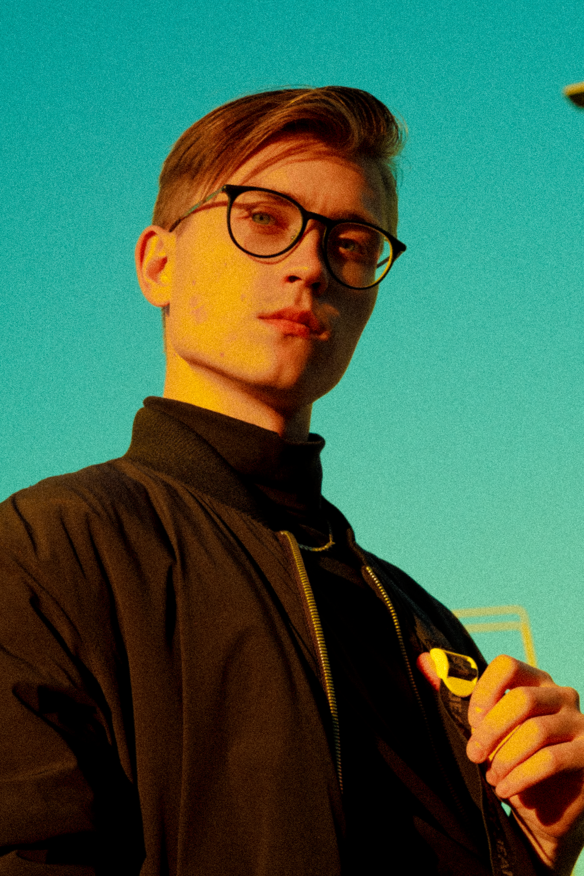A confident man in a black jacket and glasses poses against a vibrant green background.