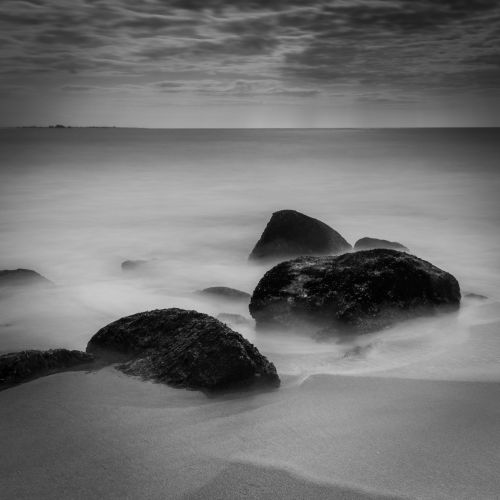 Free Serene black and white ocean scene with rocks and smooth water. Stock Photo