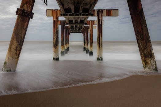 Stunning long exposure shot of waves beneath a rusty pier, capturing serene ocean movement and sandy beach.