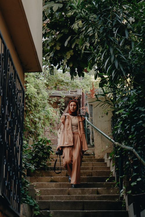 Free Elegant woman in stylish attire walks down lush, green urban steps. Stock Photo