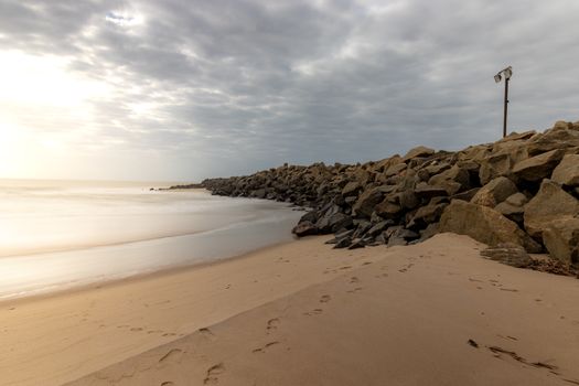 A serene beach scene with rocks and white sand under a cloudy sky.
