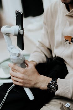 Man using a stabilizer for smartphone filming indoors, wearing a beige sweater and wristwatch.