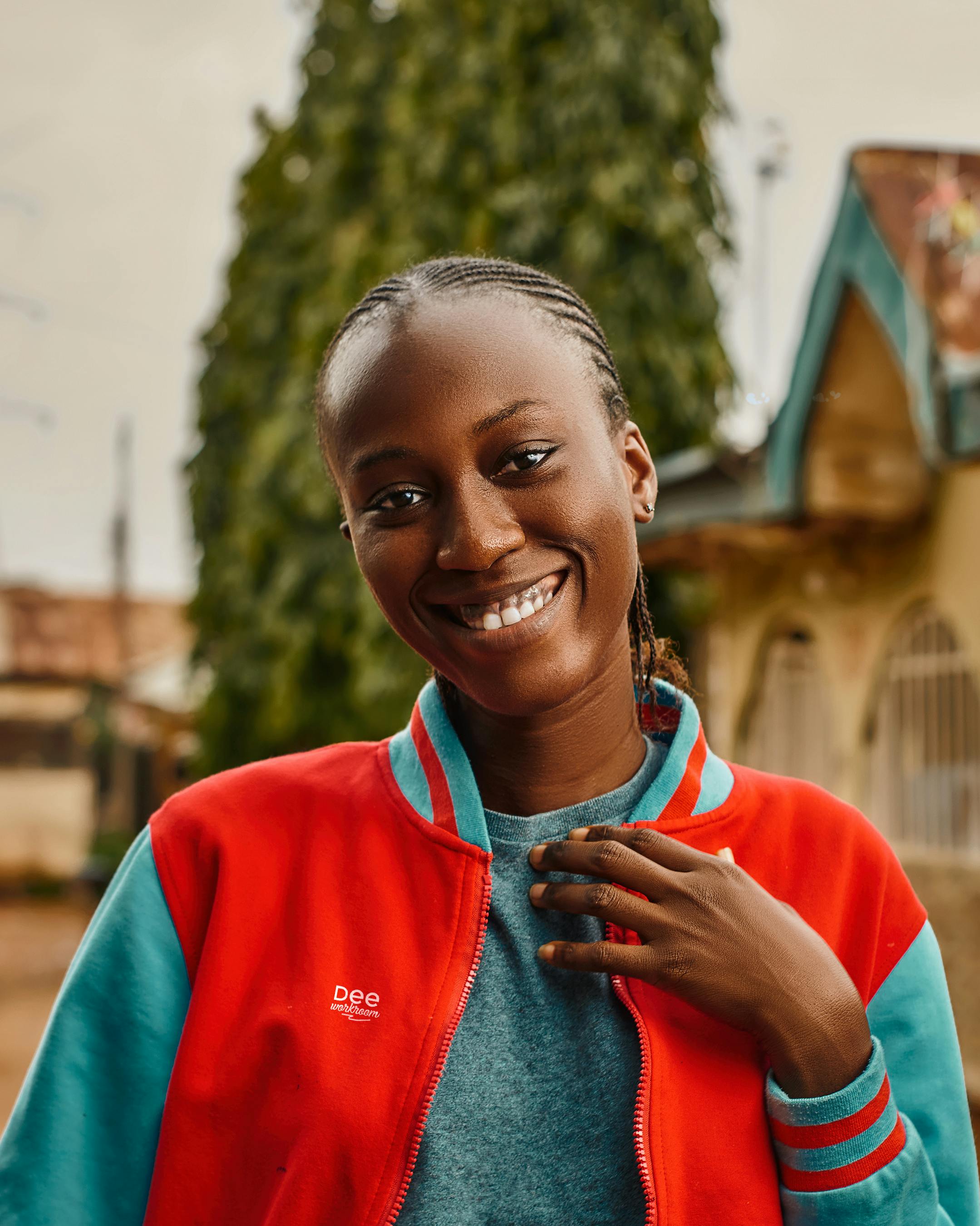 Portrait of a smiling woman in a colorful jacket, captured outdoors in Abuja, Nigeria.