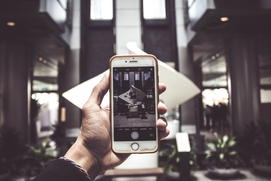 Pessoa tirando uma foto de um espaço interno moderno com o celular, destacando o uso da tecnologia na captura de ambientes contemporâneos.