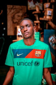 A young man in a green FC Barcelona jersey poses for a portrait indoors.