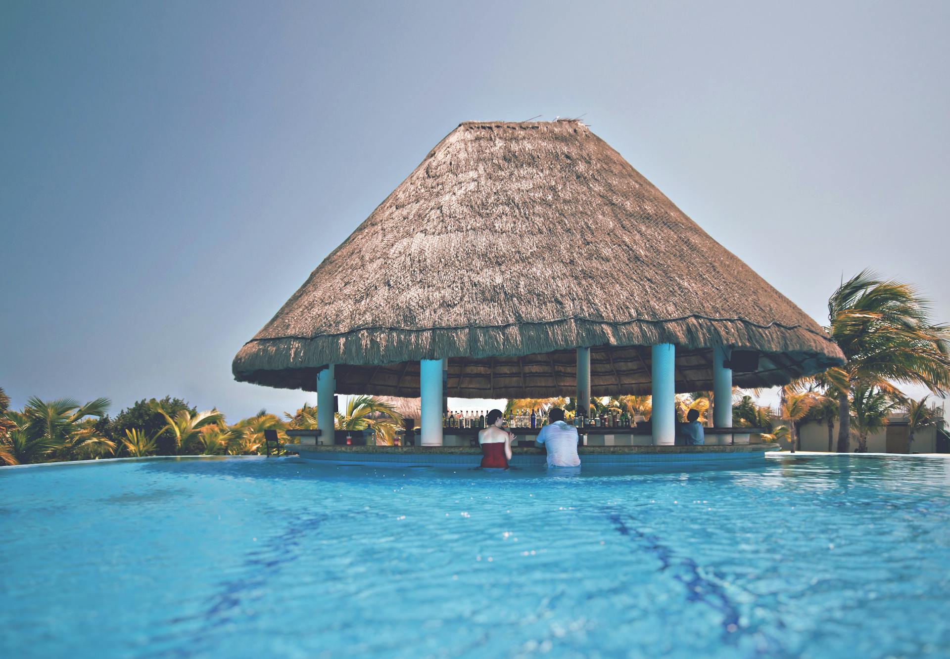 A serene poolside bar with a thatched roof provides a tropical escape at a lush resort.