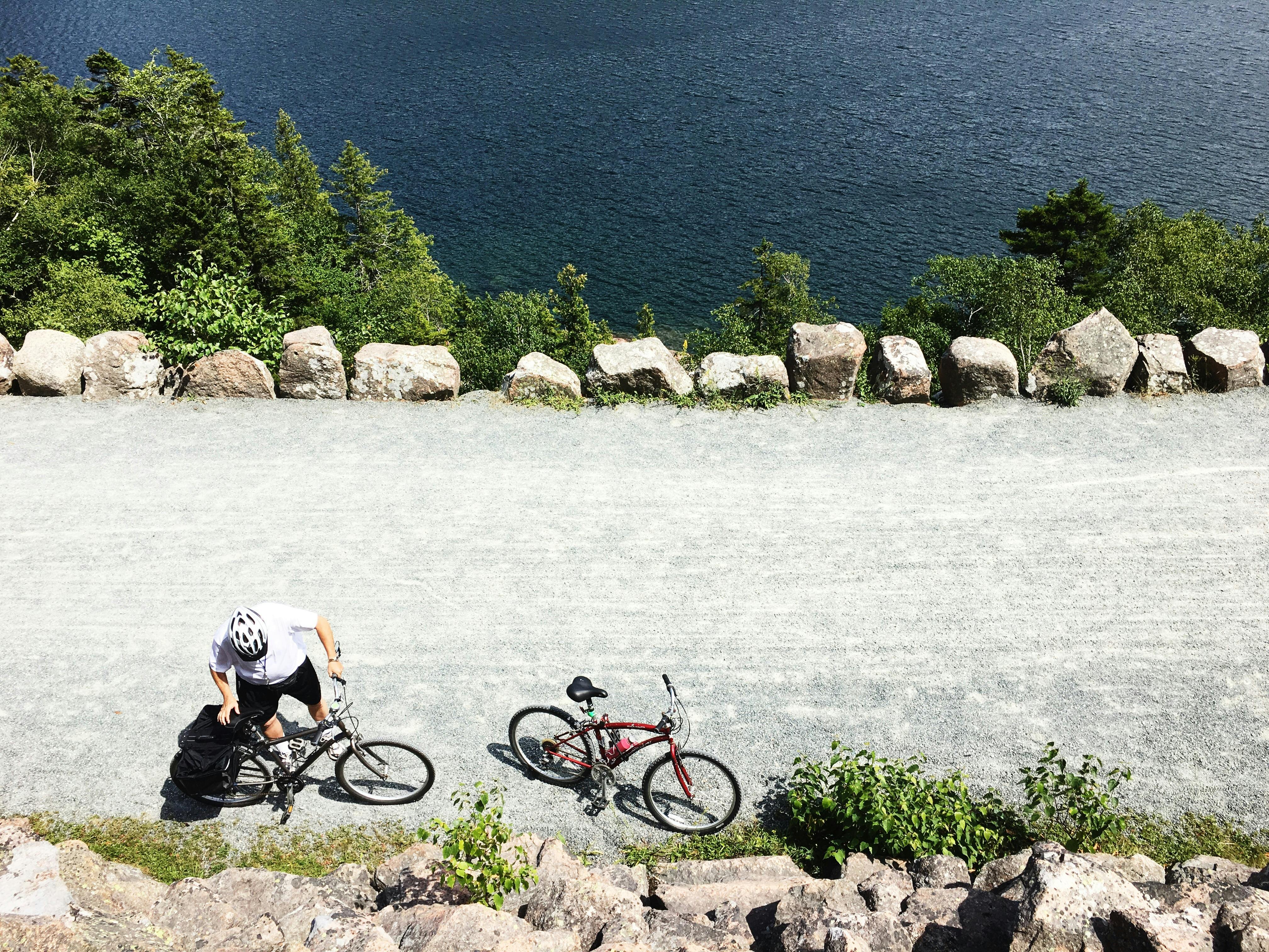 Aerial view of a cyclist resting beside a bike trail near Bar Harbor, ME, by scenic water.