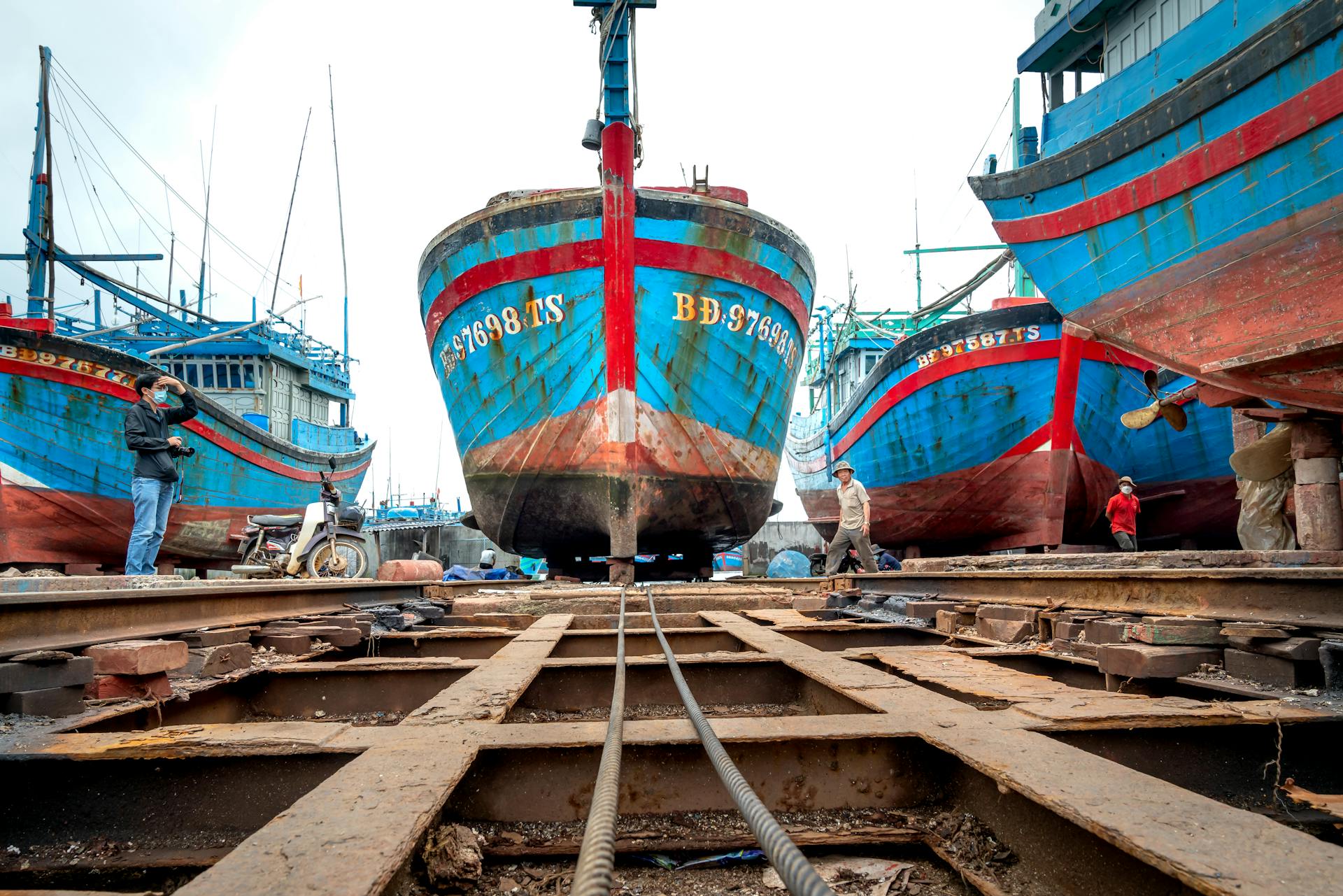 Rusty wooden fishing boats being repaired in a shipyard with visible ropes.