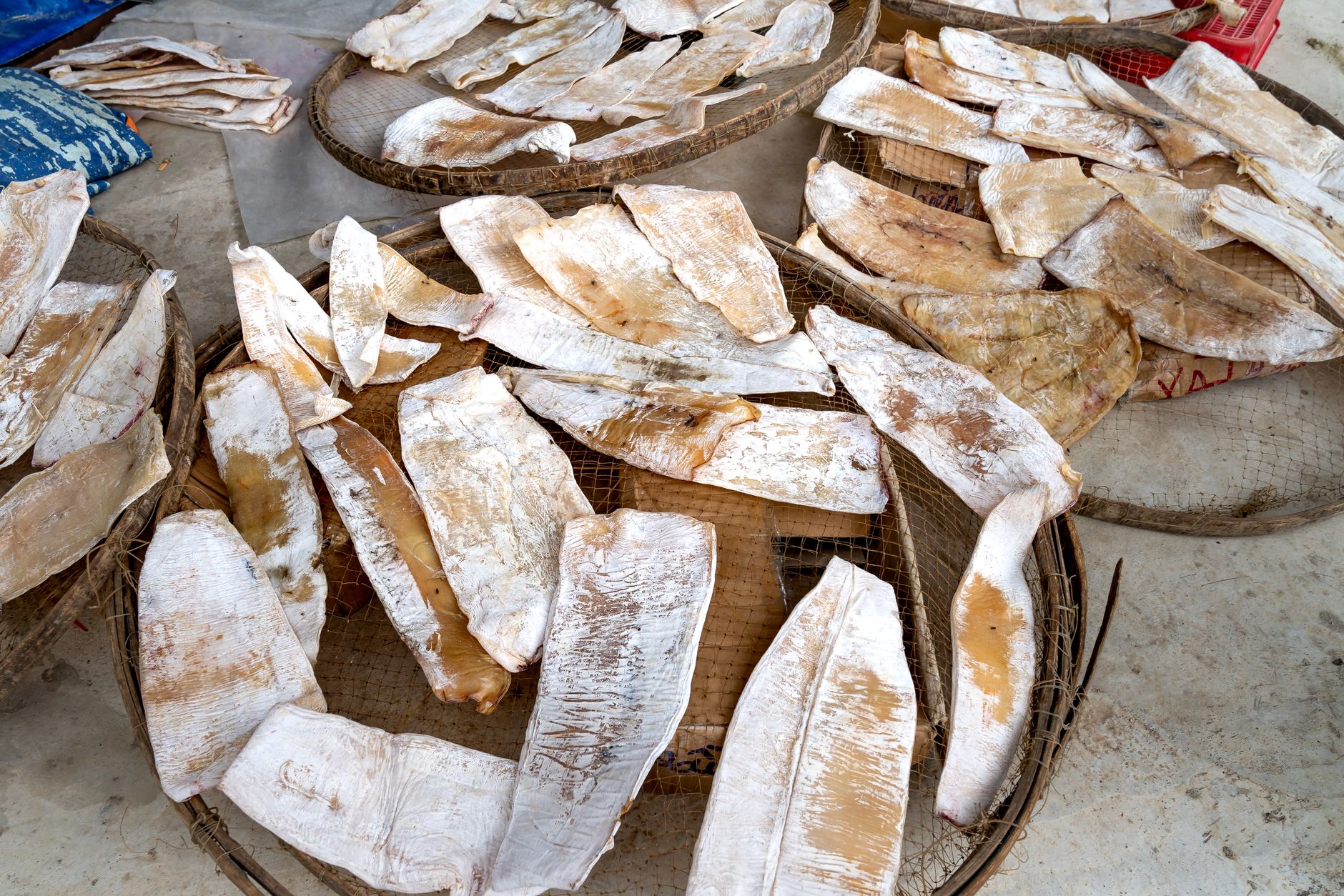 Close-up of dried fish arranged on woven trays, prepared for market sale.