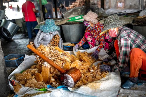 Free Three workers prepare sugar crystals at an outdoor market, wearing colorful hats and masks. Stock Photo