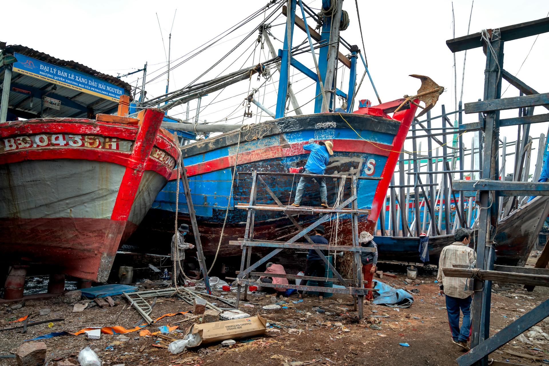 Workers repairing colorful fishing boats in a busy dockyard, focusing on teamwork and craftsmanship.