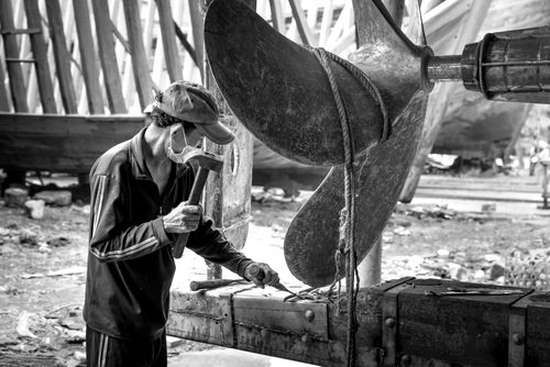 Free A shipyard worker hammering a large propeller in a black and white setting. Stock Photo