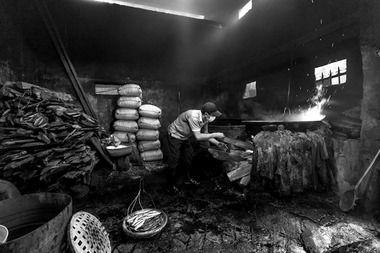 Black And White Photo Of A Fisherman Smoking Fish In A Barn