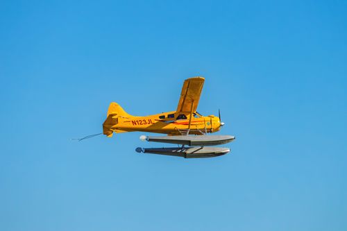 Free Vibrant yellow seaplane flying against a clear blue sky, showcasing aviation freedom. Stock Photo
