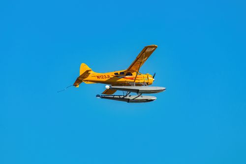 Free A vibrant yellow seaplane flying against a clear blue sky, showcasing dynamic flight and aerodynamics. Stock Photo