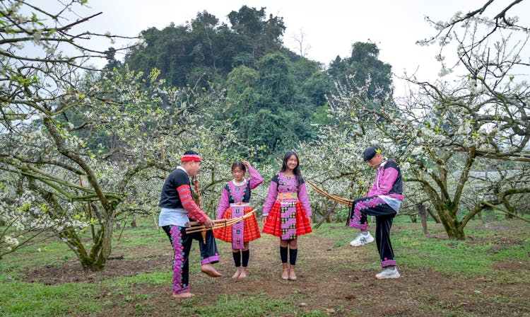 Young People Wearing Traditional Clothing Standing In A Blossoming Orchard