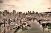 在城市港口的多云天空下，充满活力的码头边停靠着船只，周围矗立着摩天大楼