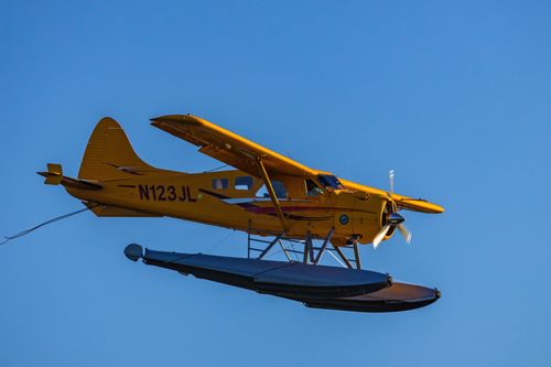 Free A vibrant yellow seaplane soars against a clear blue sky. Stock Photo