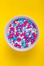 一个白色碗里装满了彩色糖果，背景是鲜艳的黄色，非常适合食品促销