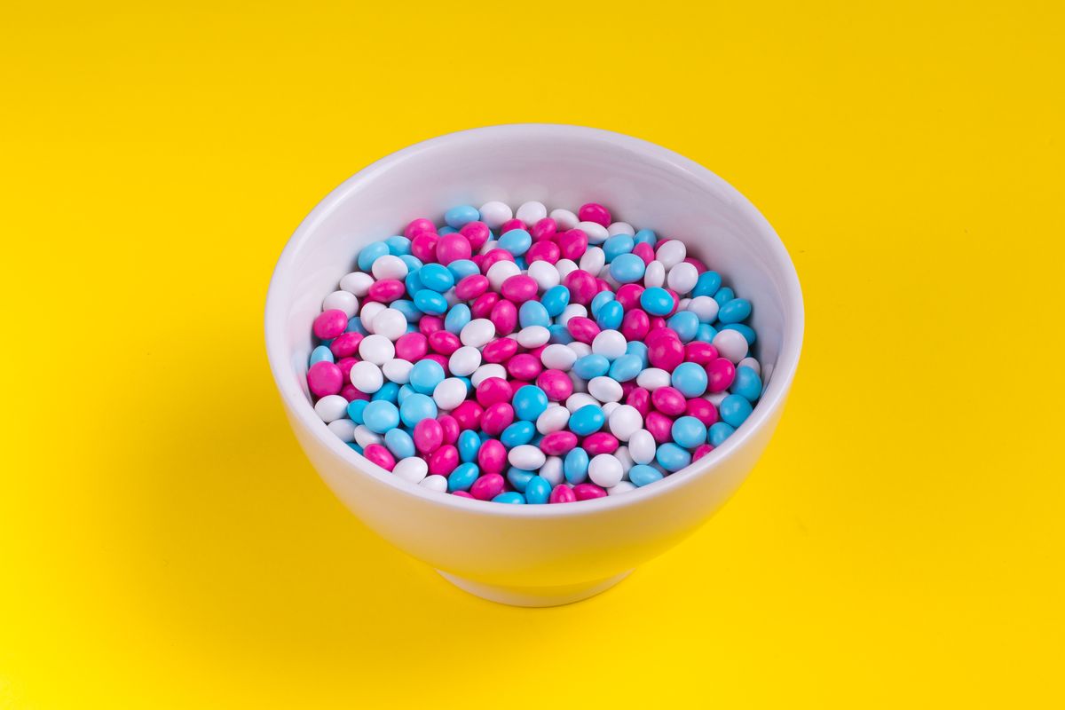 Close-up of colorful candies in a white bowl against a bright yellow background.