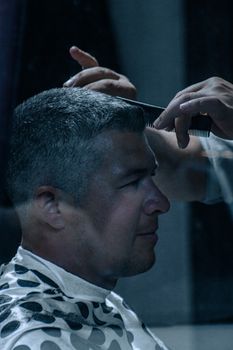 Close-up side view of a barber combing a client's hair in a stylish indoor setting.