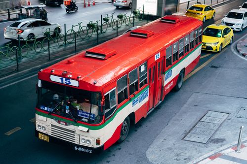 Free A red public bus travels city streets surrounded by taxis and cars, showcasing urban transportation. Stock Photo