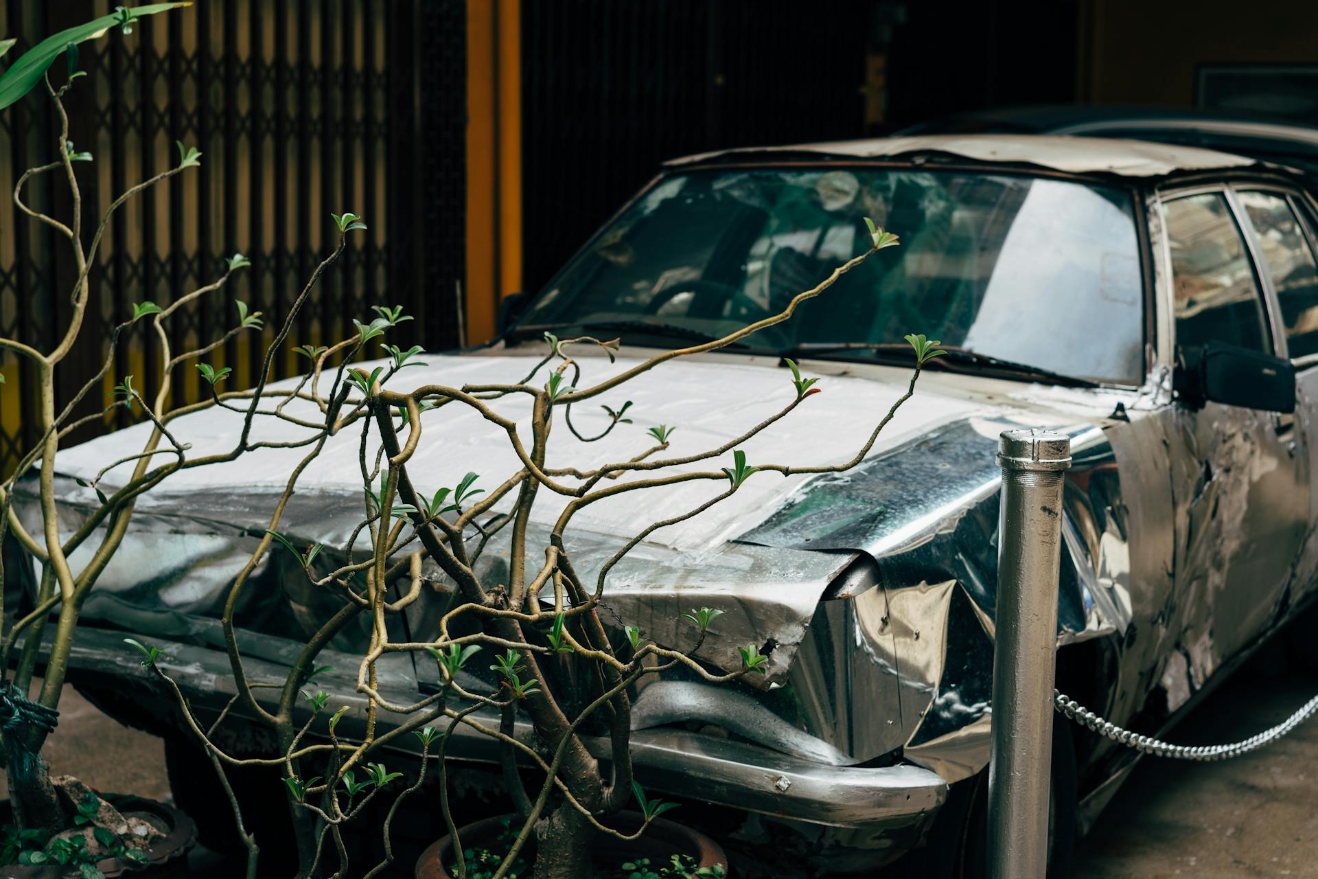 An abandoned vintage car with visible damage amidst an urban street setting.