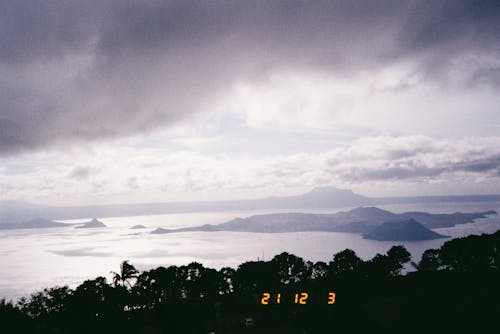 Silhouette of Trees Overlooking Small Volcano on Body of Water During Sunset