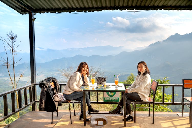 Two Women Drinking Orange Juice On A Terrace With A Mountain View