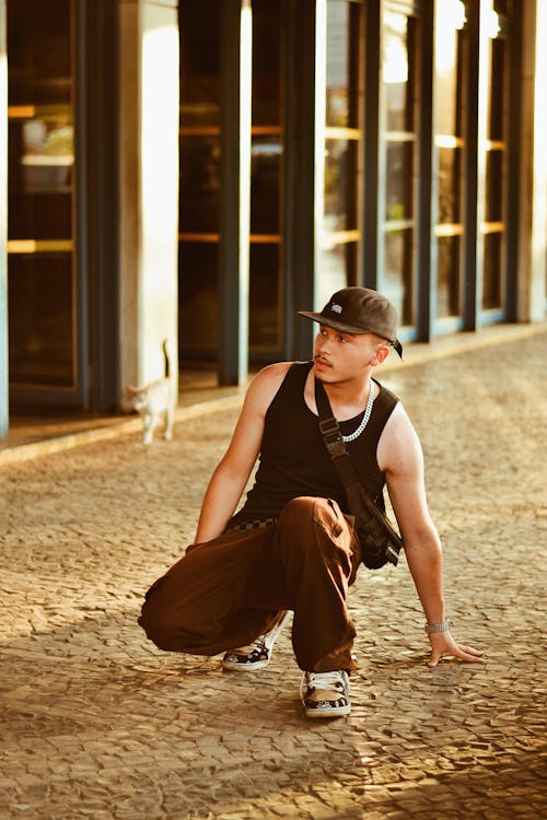 Man in Black Tank Top Squatting on Stone Pavement