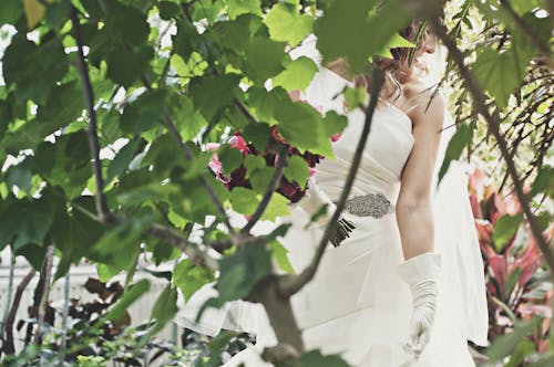緑の木々の近くで白いウェディングドレスを着ている女性
