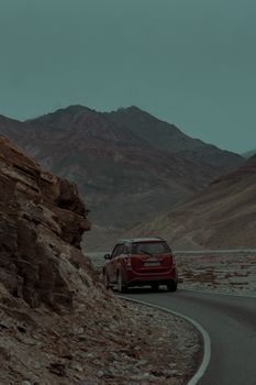 Red SUV navigating a scenic, winding road amidst mountain landscape in a deserted region.
