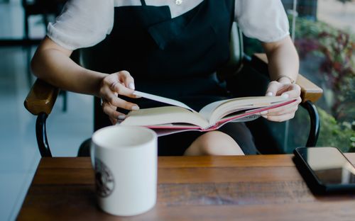 Free A woman reading a book and enjoying a coffee in a cozy indoor café setting, relaxed atmosphere. Stock Photo