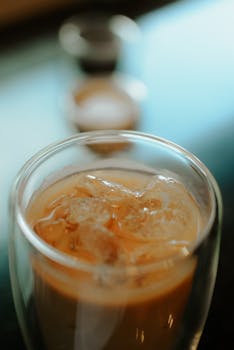 Close-up view of iced coffee in a clear glass cup with ice cubes, perfect for a refreshing break.