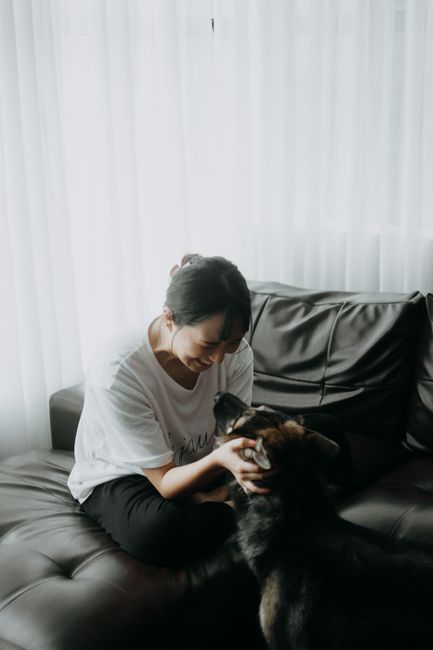 Asian woman affectionately interacting with her German Shepherd dog on a comfortable sofa indoors.