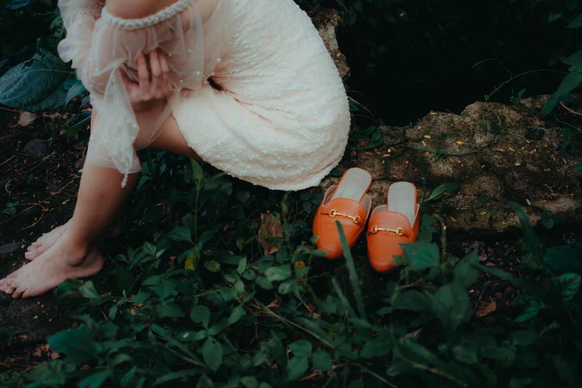 A woman in a beaded dress sitting beside brown mules — the elegant mule