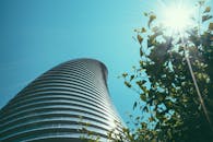 在清澈的蓝天映衬下，现代弧形摩天大楼以低角度呈现，太阳耀斑与绿叶点缀其间