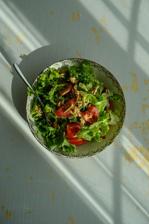 Free A vibrant and healthy salad featuring fresh lettuce, tomatoes, and walnuts on a sunlit table. Stock Photo