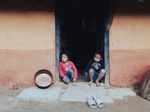 Free Two children sitting outside the doorway of a rural home, reflecting a quiet moment. Stock Photo