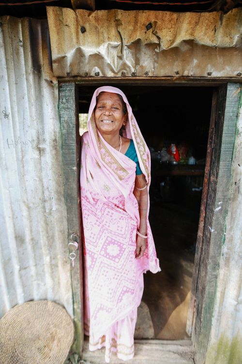 Free Joyful woman in a pink sari stands smiling at a rustic doorway, exuding warmth and welcome. Stock Photo