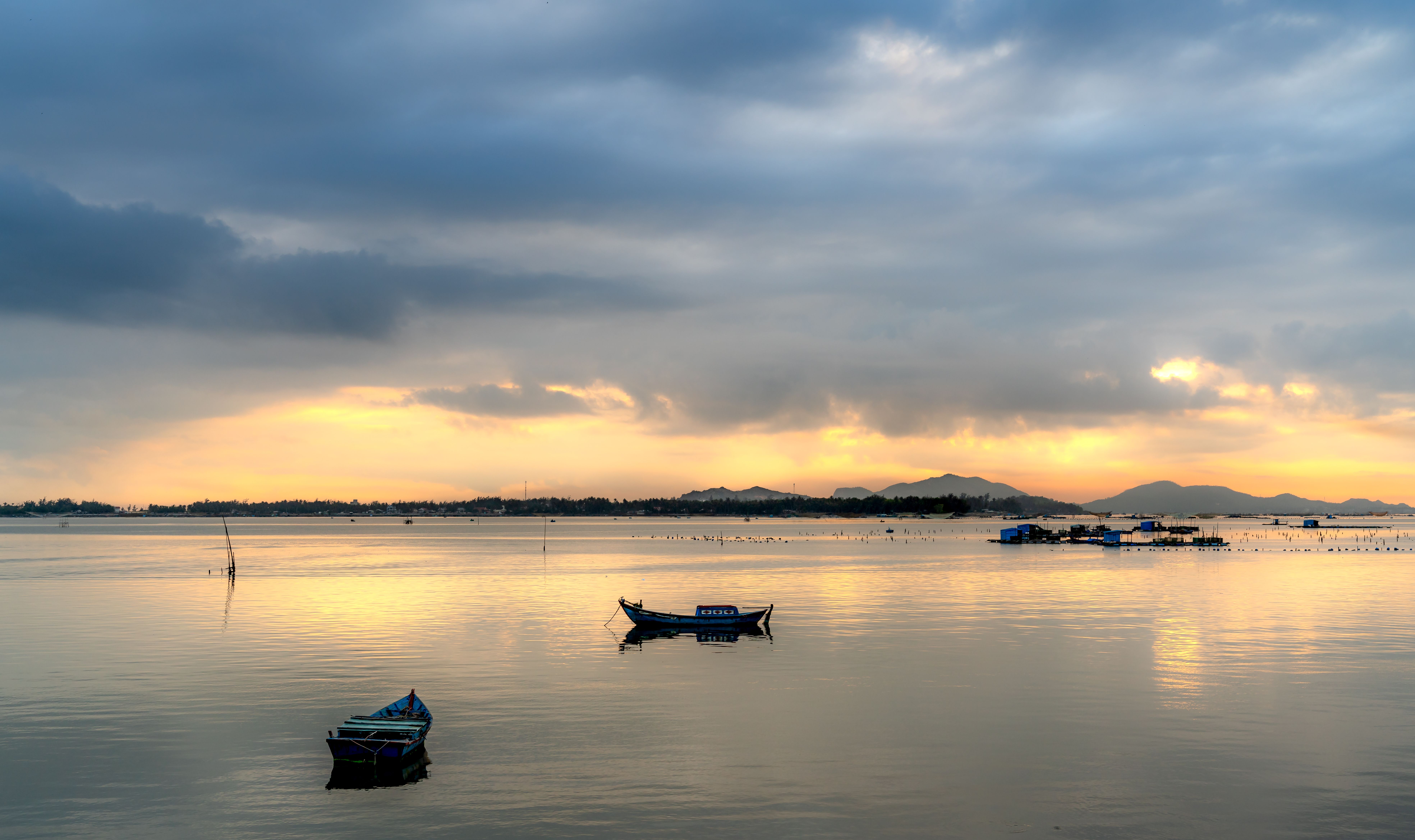 Peaceful sunset scene with boats floating on a calm lake under a cloudy sky